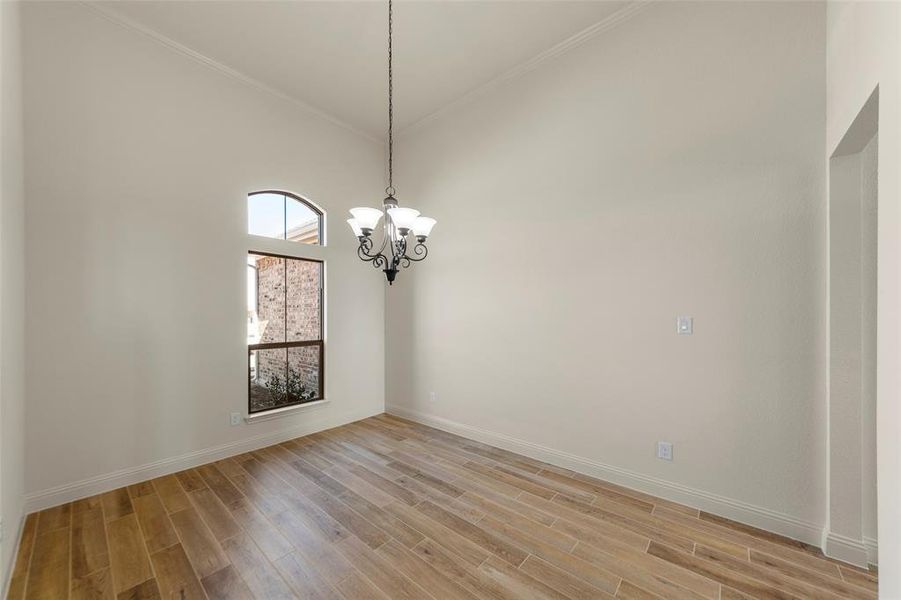 Empty room with wood tiled floors, suspended lighting, a high ceiling, and crown molding Empty room with wood tiled floors, suspended lighting, a high ceiling, and crown molding