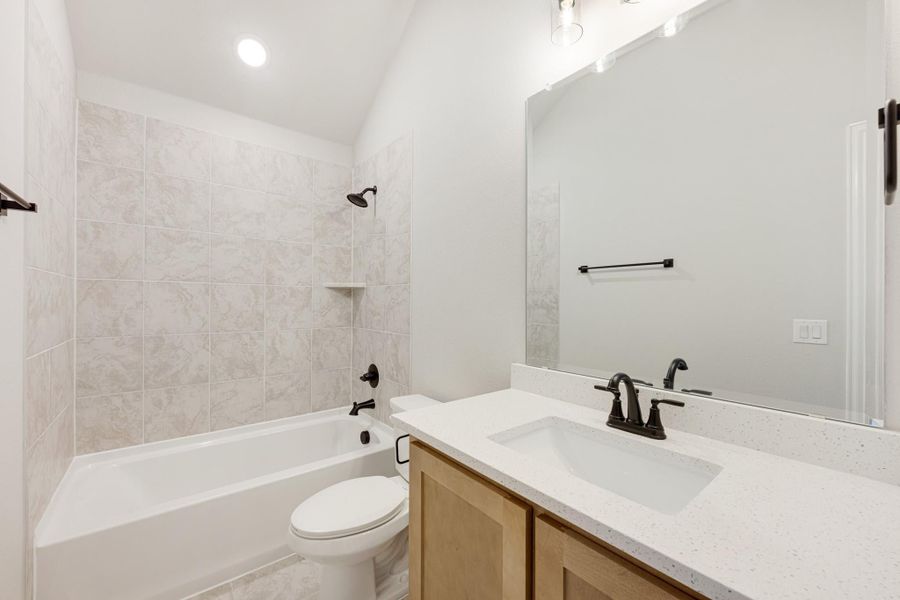Bathroom with tiled tub-shower combo, white quartz vanity, wood cabinets, and vaulted ceiling