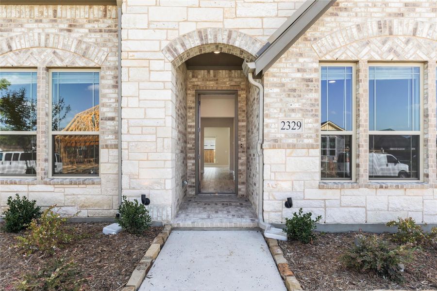 Front entry of home with arched brick doorway, stone exterior, and concrete walkway leading to open door