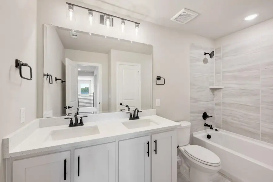 Bathroom with double vanity, white quartz countertop, and tiled shower-tub combo with black fixtures Bathroom with double vanity, white quartz countertop, and tiled shower-tub combo with black fixtures
