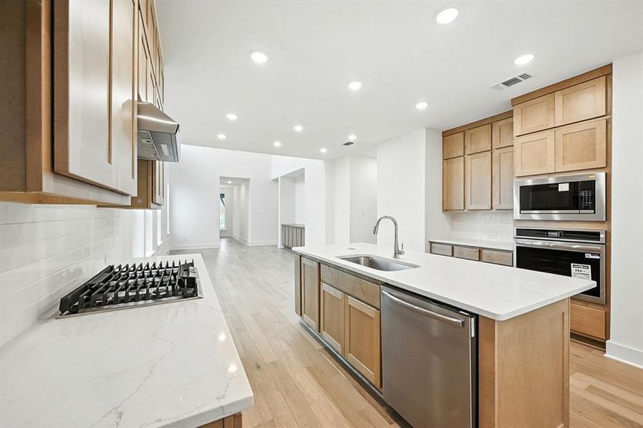 Kitchen with backsplash, stainless steel appliances, light stone countertops, a kitchen island with sink, and recessed lighting Kitchen with backsplash, stainless steel appliances, light stone countertops, a kitchen island with sink, and recessed lighting