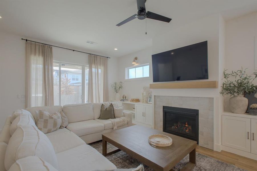 Living room featuring a tiled fireplace, ceiling fan, and light hardwood / wood-style flooring