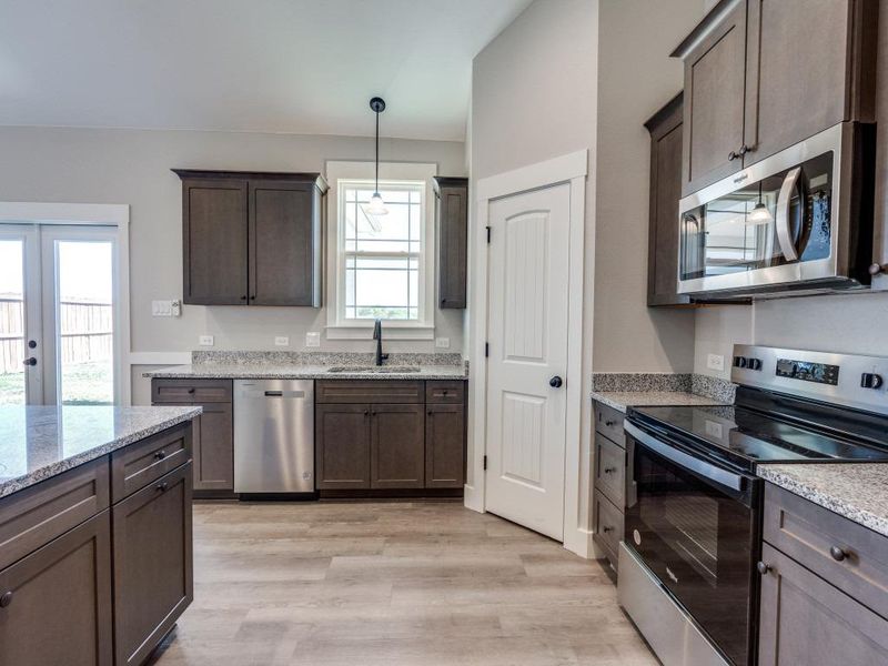 Kitchen featuring light wood finished floors, a sink, dark brown cabinets, decorative light fixtures, and appliances with stainless steel finishes