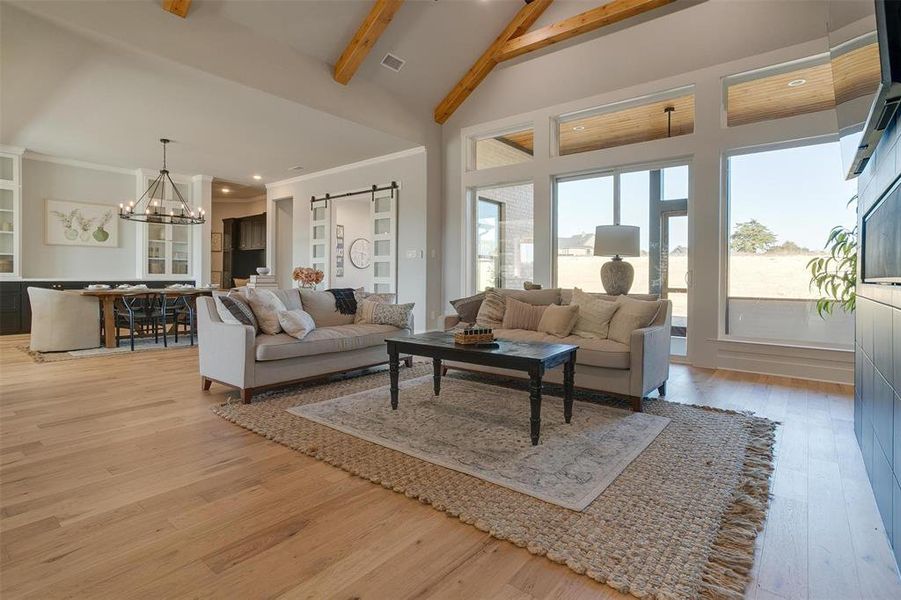 Living room with beam ceiling, a barn door, high vaulted ceiling, a chandelier, and light wood-type flooring