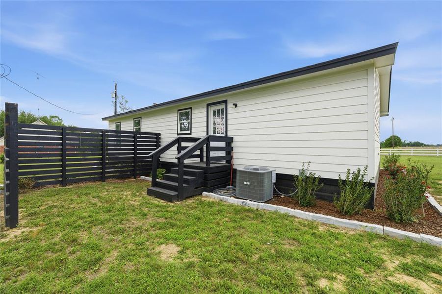 Exterior featuring white horizontal siding, black trim, a sloped black roof, a black horizontal slat fence, and a black deck with steps