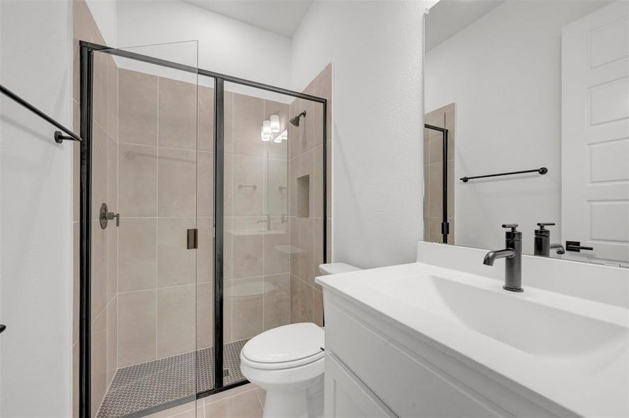 Bathroom featuring a glass-enclosed shower with tiled walls and a dark tiled floor, a white vanity with a rectangular sink, and a large mirror