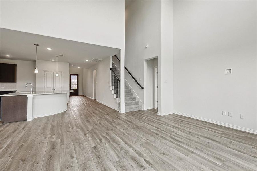 Unfurnished living room featuring a towering ceiling, sink, and light wood-type flooring