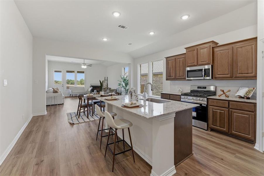 Kitchen with a center island featuring a sink, stainless steel appliances, wood-finish cabinetry, and light-toned countertops