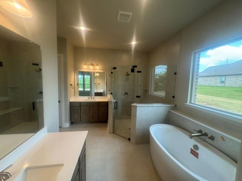 Expansive bathroom featuring a freestanding soaking tub, a large glass-enclosed shower with a built-in bench, dual vanity with wood cabinetry, and a large window