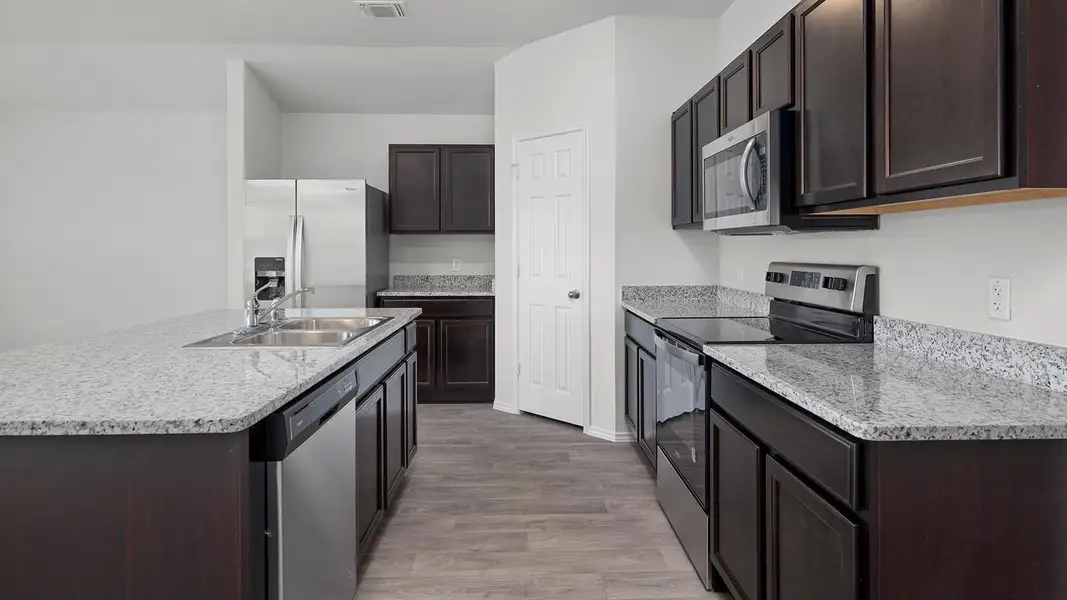 Kitchen with stainless steel appliances, dark brown cabinetry, a kitchen island with sink, and light stone counters
