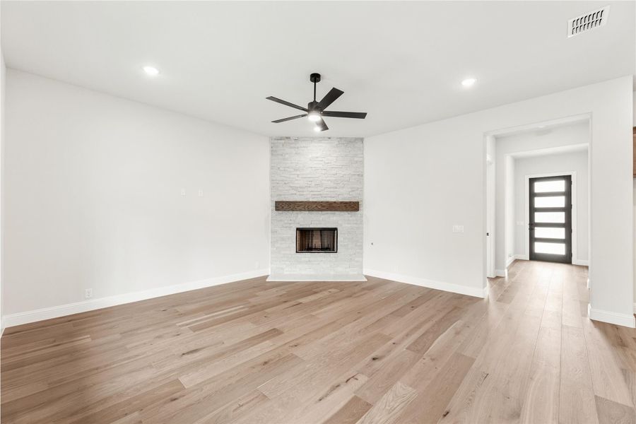 Open living room with stone fireplace, wood mantel, ceiling fan, and light hardwood floors