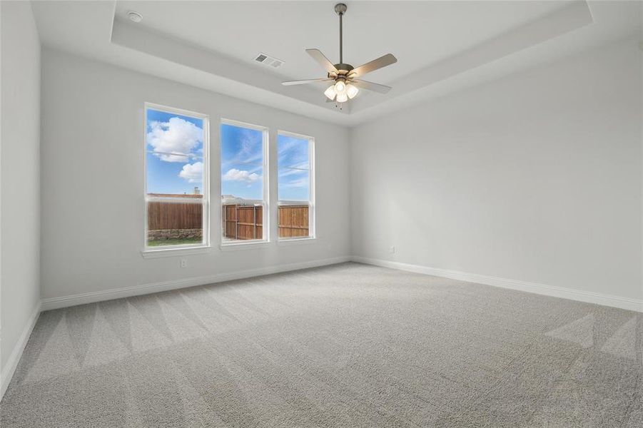 Carpeted spare room featuring ceiling fan, a tray ceiling, visible vents, and baseboards Carpeted spare room featuring ceiling fan, a tray ceiling, visible vents, and baseboards