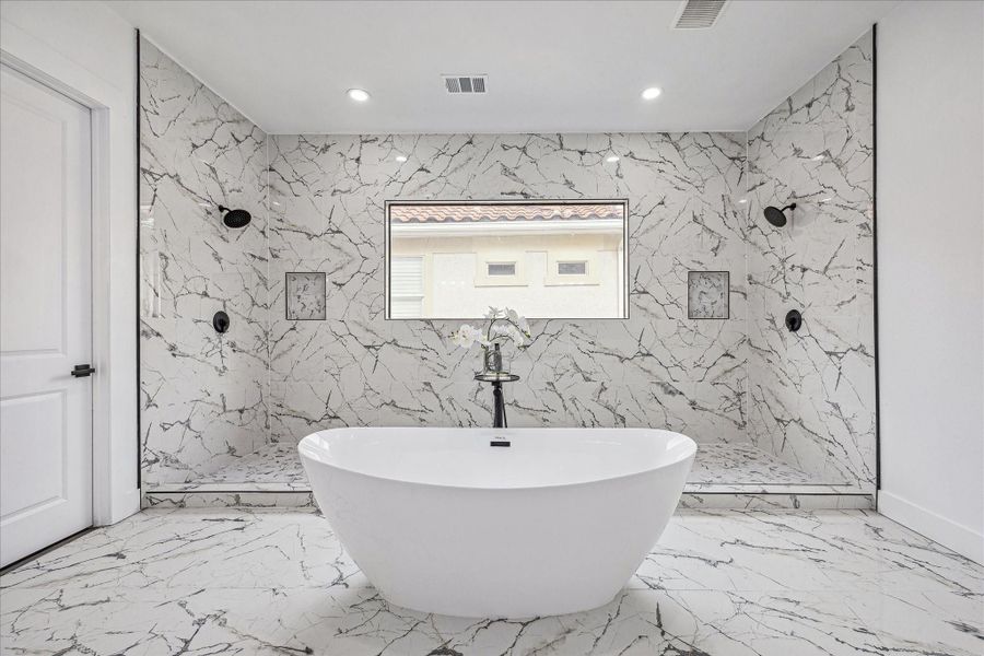 From this angle, the light-filled primary bathroom reveals its spa-like design, showcasing elegant marble, dual showers, and the relaxing soaking tub.