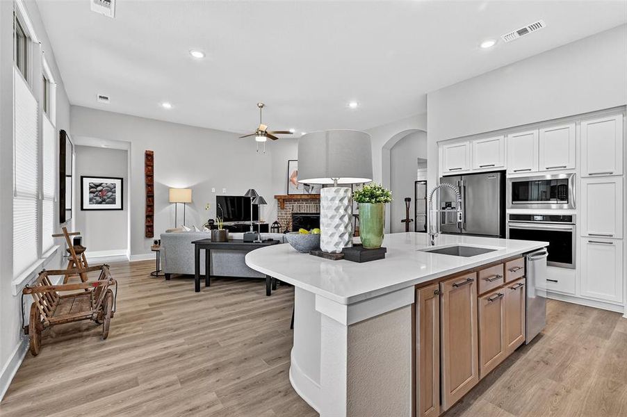 Kitchen with stainless steel appliances, ceiling fan, a fireplace, light wood-style floors, and arched walkways Kitchen with stainless steel appliances, ceiling fan, a fireplace, light wood-style floors, and arched walkways