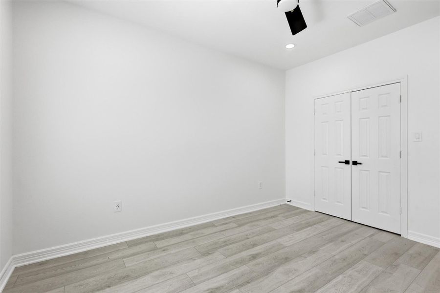 Second floor bedroom with ceiling fan, white walls, and light wood look floors.