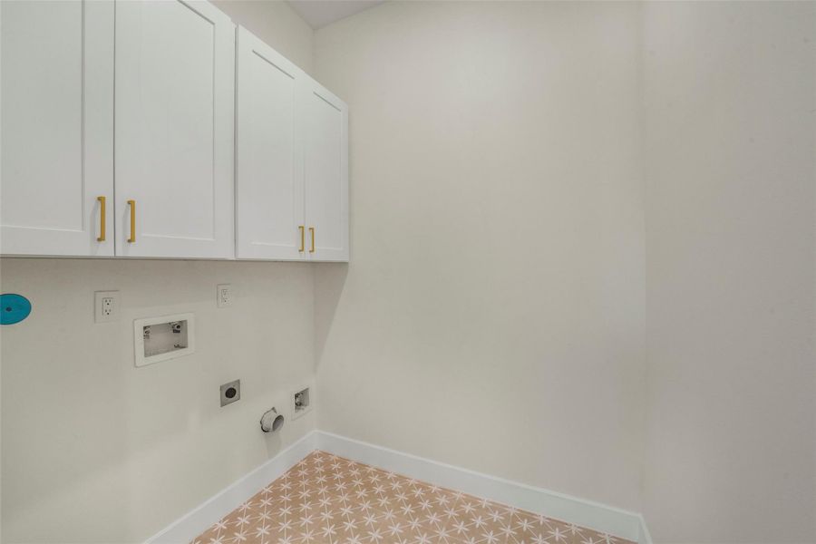 This photo shows a laundry room with white cabinets featuring gold handles, hook-ups for washer and dryer, and star-patterned tile flooring. The walls are painted a light, neutral color.