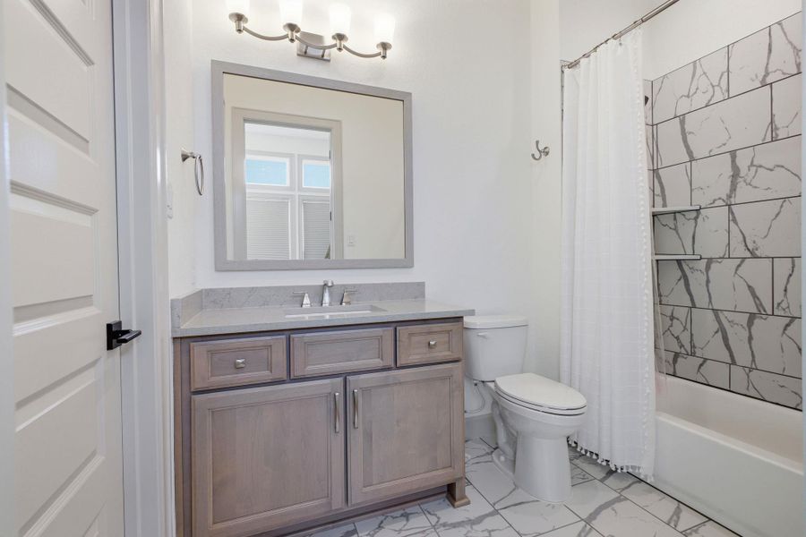 Bathroom featuring a vanity with a light gray countertop, a shower with white and gray tiled walls, a white toilet, and tile flooring