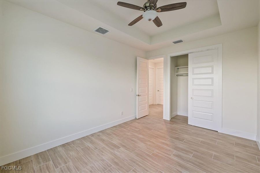 Unfurnished bedroom featuring a raised ceiling, wood finish floors, a closet, and ceiling fan