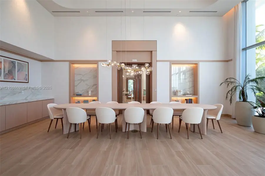 Double-height ceilings featuring recessed lighting, floor-to-ceiling windows, light wood-finish flooring, custom built-in cabinetry with stone slab accents, and a sculptural multi-globe pendant light fixture