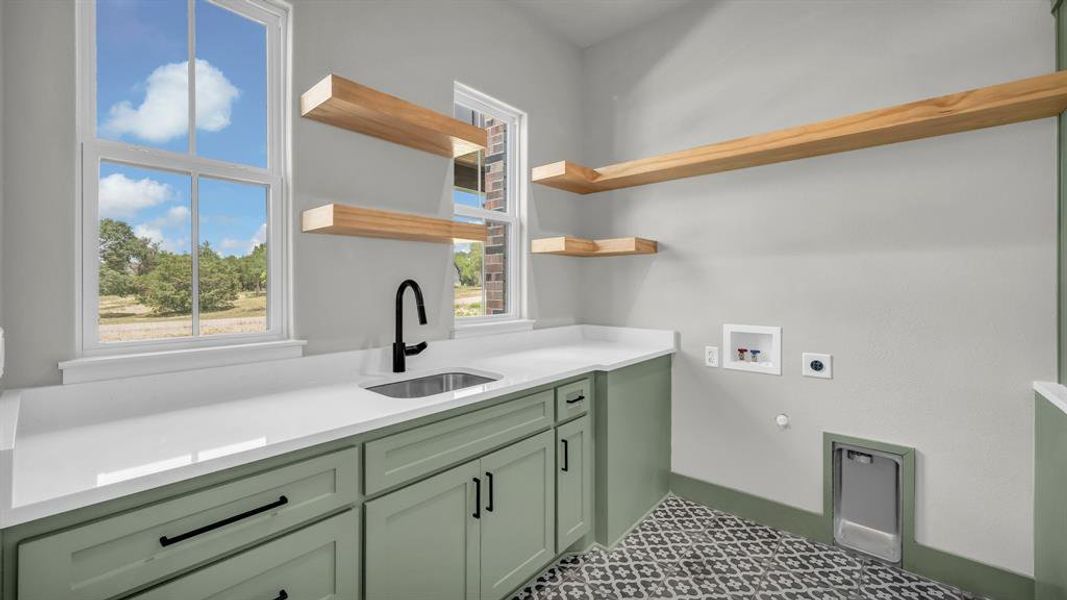 Utility room featuring light green cabinetry with black hardware, white countertops, a stainless steel sink with a matte black faucet, and patterned floor tiling
