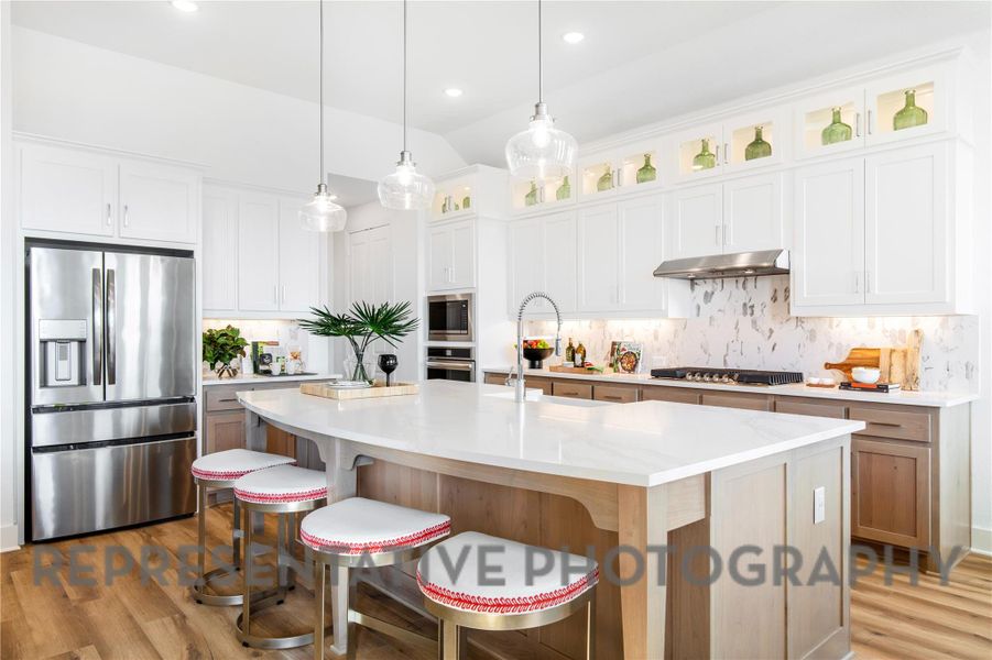 Kitchen with wood finished floors, under cabinet range hood, glass insert cabinets, stainless steel appliances, and an island with sink Kitchen with wood finished floors, under cabinet range hood, glass insert cabinets, stainless steel appliances, and an island with sink