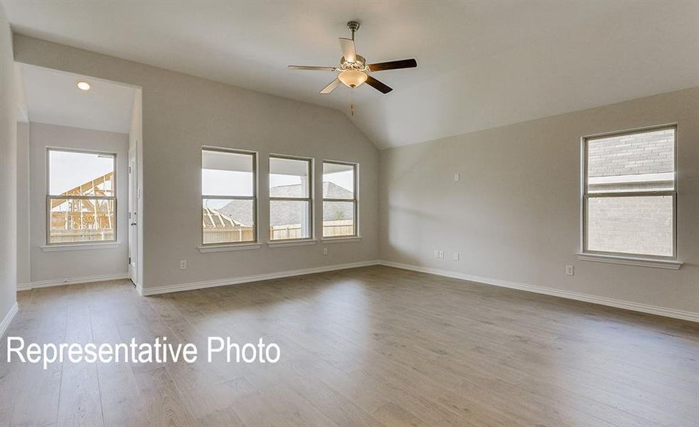 Spacious interior featuring wood-finish flooring, vaulted ceilings, a ceiling fan, and multiple windows providing natural light