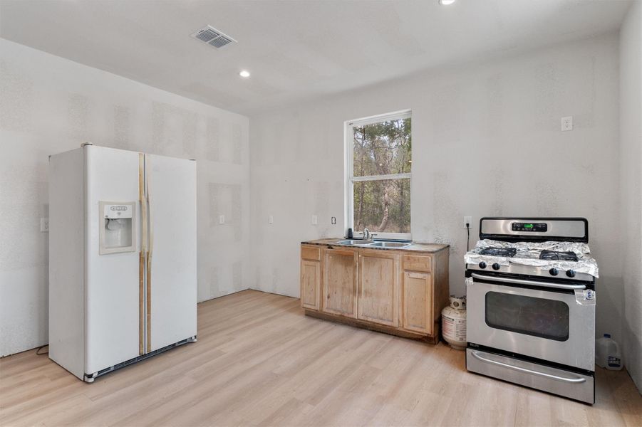 Kitchen featuring gas range, white refrigerator with ice dispenser, light wood-style floors, recessed lighting, and light brown cabinetry Kitchen featuring gas range, white refrigerator with ice dispenser, light wood-style floors, recessed lighting, and light brown cabinetry