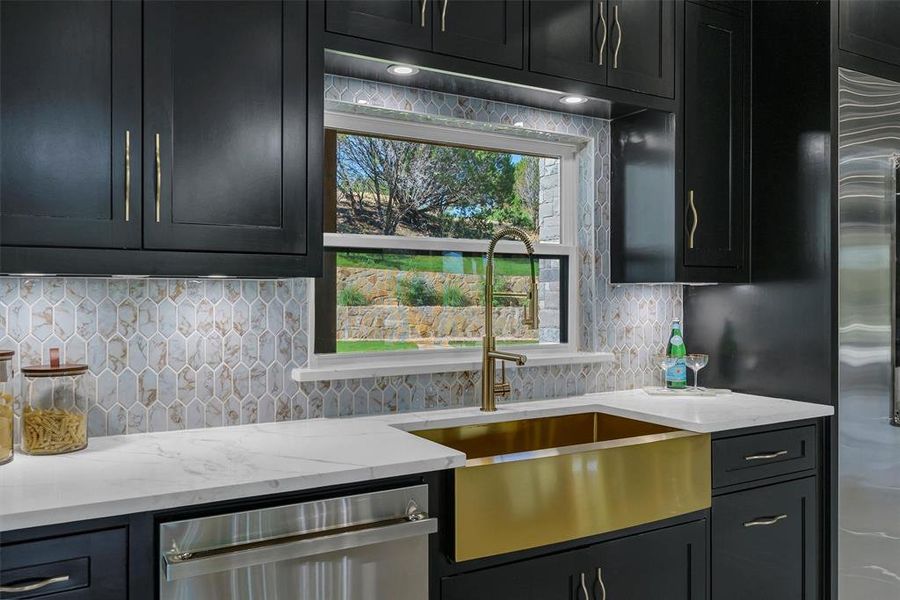 Kitchen featuring stainless steel dishwasher, sink, light stone countertops, and backsplash