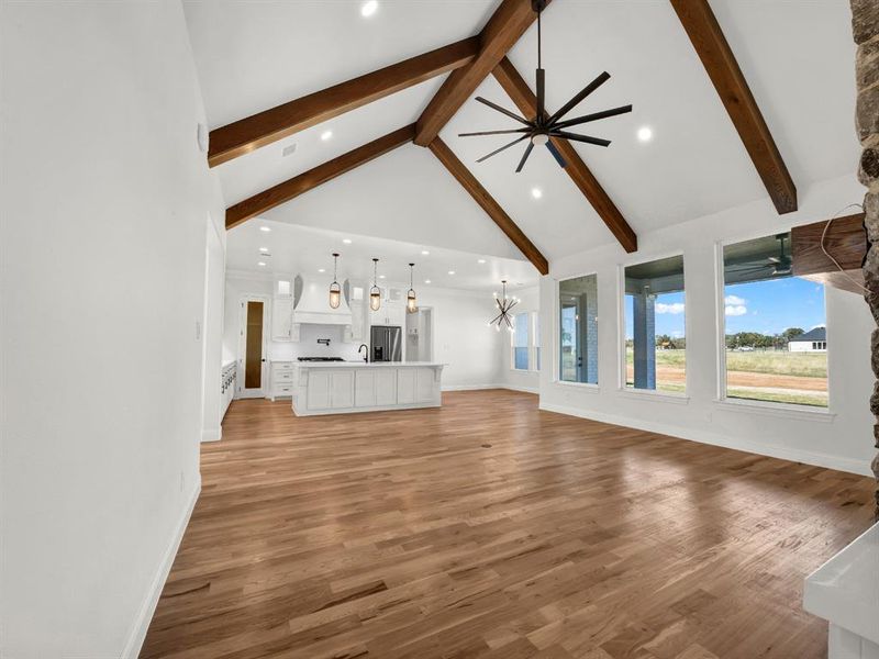 Unfurnished living room with beam ceiling, light hardwood / wood-style flooring, and high vaulted ceiling