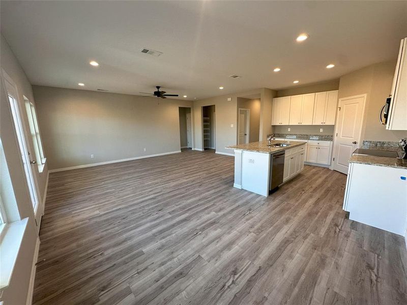 Kitchen with hardwood / wood-style floors, stainless steel appliances, light stone counters, ceiling fan, and a center island with sink