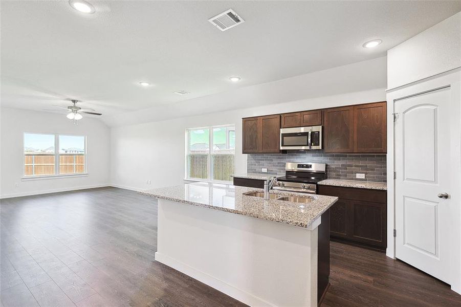 Kitchen featuring stainless steel appliances, dark hardwood / wood-style flooring, sink, ceiling fan, and a center island with sink