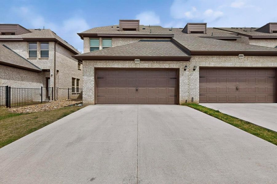 The property features a light-colored brick exterior with brown garage doors and a grey roof