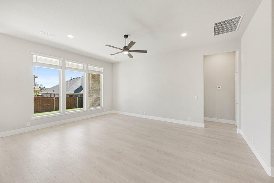 Empty living room with light wood floors, ceiling fan, and large windows overlooking backyard