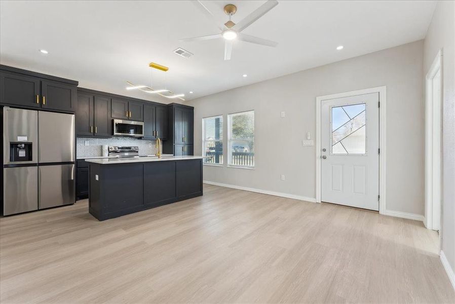 Kitchen featuring stainless steel appliances, light countertops, visible vents, backsplash, and light wood-type flooring