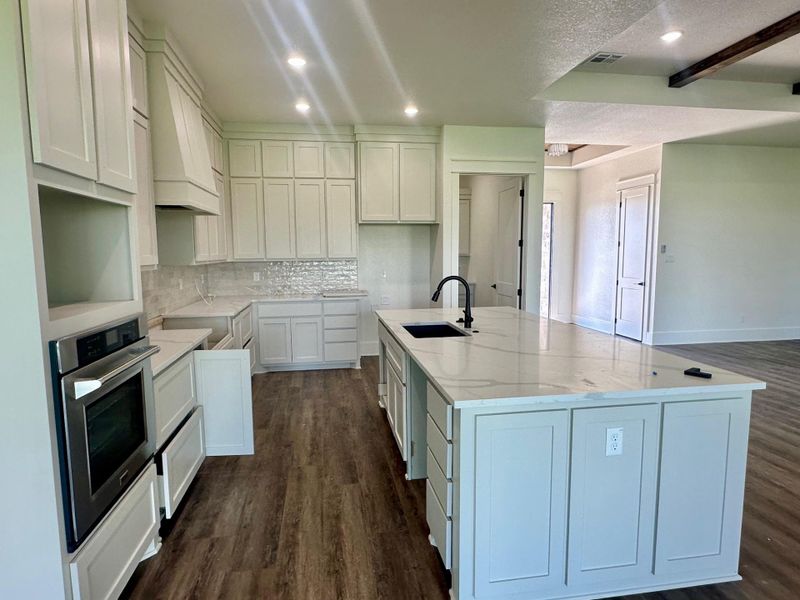 Kitchen with light stone counters, a center island with sink, dark wood-style flooring, stainless steel oven, and recessed lighting