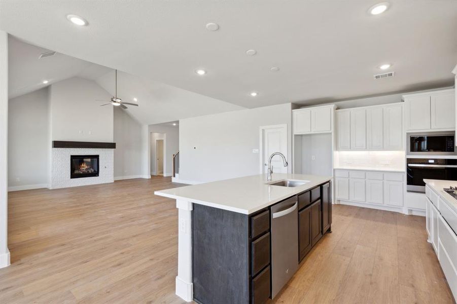 Kitchen featuring light wood-type flooring, a kitchen island with sink, black appliances, vaulted ceiling, and sink