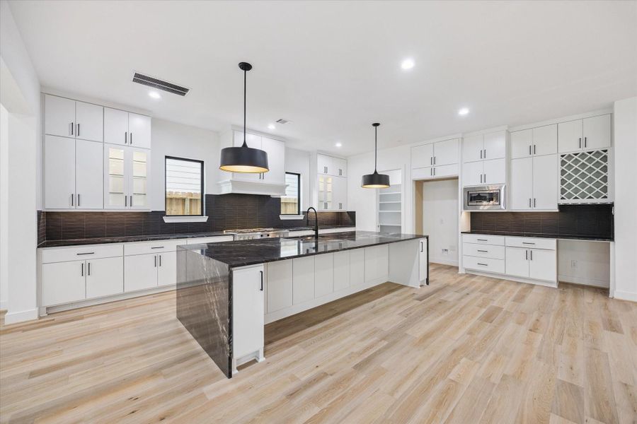 Bold contrast and streamlined design define this chef-worthy kitchen, featuring a dramatic waterfall-edge island, black tile backsplash, and modern pendant lighting. Ample cabinetry, a built-in wine rack, and pantry offer form and function. Bold contrast and streamlined design define this chef-worthy kitchen, featuring a dramatic waterfall-edge island, black tile backsplash, and modern pendant lighting. Ample cabinetry, a built-in wine rack, and pantry offer form and function.
