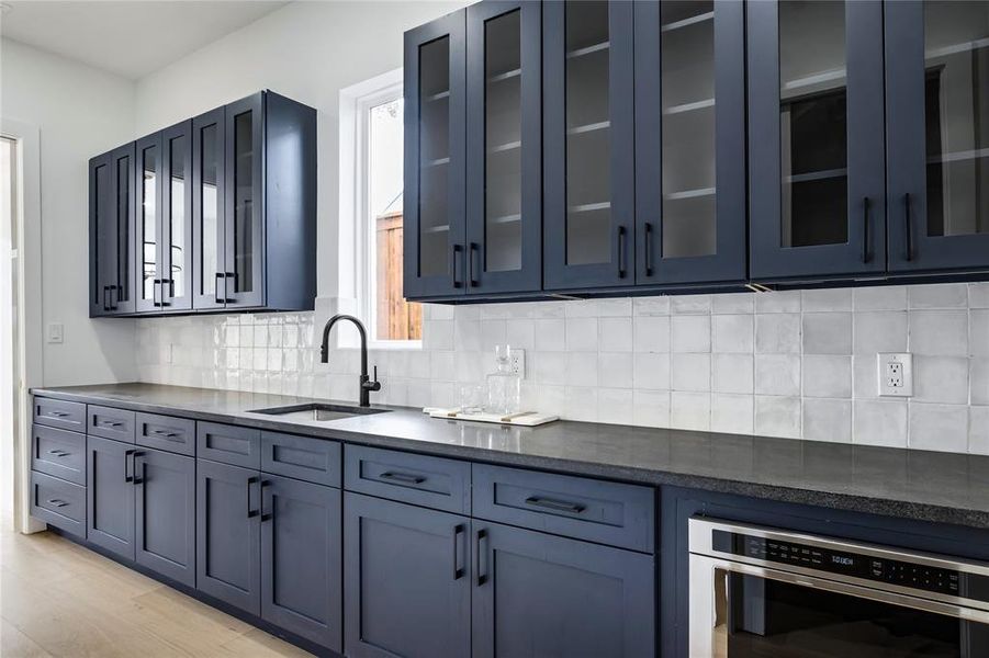 Kitchen featuring blue cabinets, sink, stainless steel oven, light hardwood / wood-style floors, and backsplash