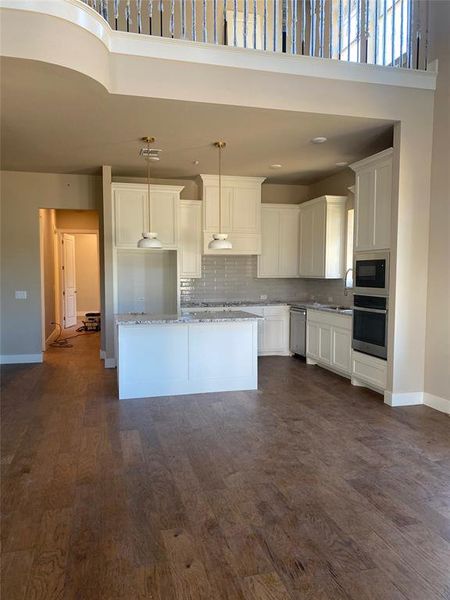 Kitchen featuring light stone counters, a towering ceiling, stainless steel appliances, white cabinetry, and decorative light fixtures