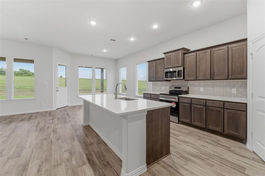 Kitchen featuring a center island with sink, wood-finish flooring, recessed lighting, and ample cabinetry