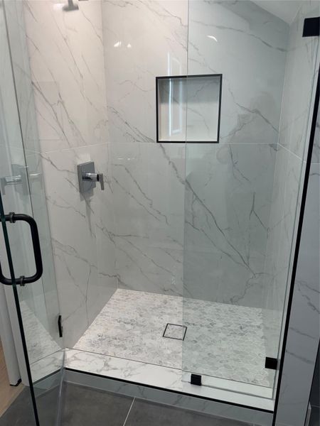 Glass-enclosed shower with large format marble-look tile walls, a built-in shower niche, and a contrasting mosaic tile floor