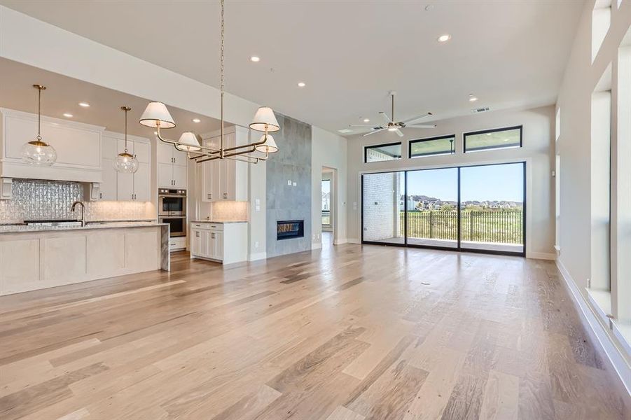 Unfurnished living room with ceiling fan with notable chandelier, a fireplace, light hardwood / wood-style floors, sink, and a towering ceiling