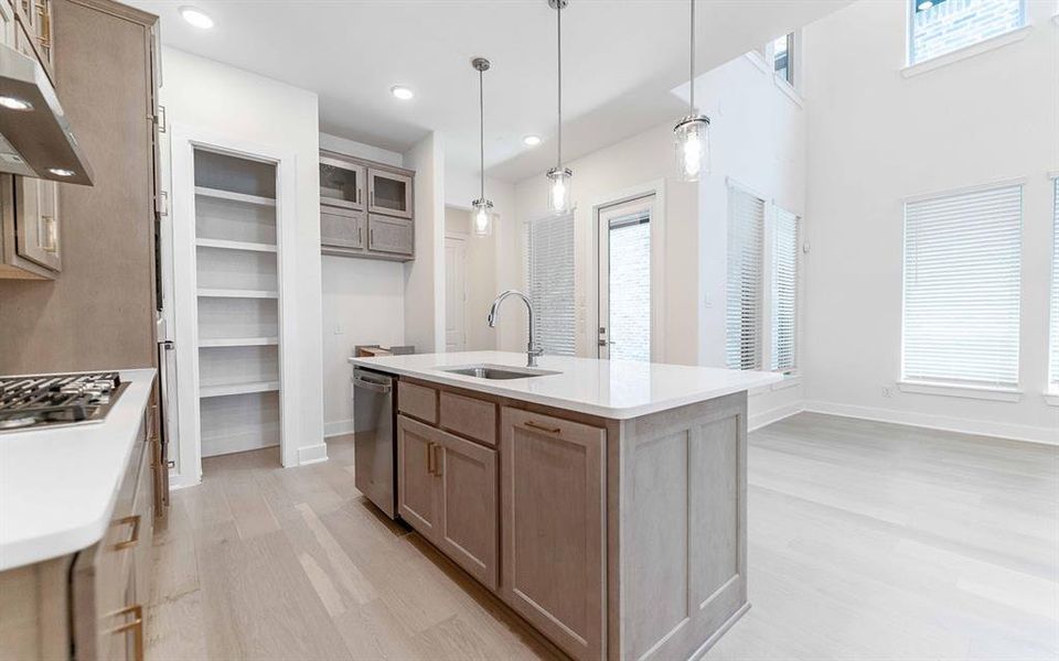 Modern kitchen featuring an island with a stainless steel sink, contemporary pendant lighting, light wood-finish flooring, ample white cabinetry, and a gas cooktop