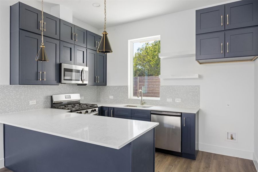 Kitchen featuring dark wood-type flooring, light stone counters, a peninsula, and stainless steel appliances Kitchen featuring dark wood-type flooring, light stone counters, a peninsula, and stainless steel appliances