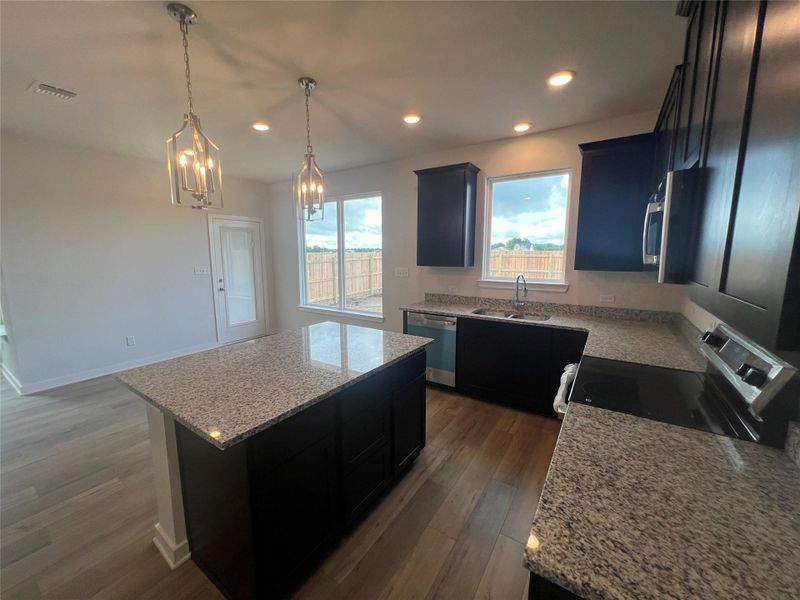 Elegant pendant lighting illuminates a modern kitchen featuring rich cabinetry and durable granite countertops.