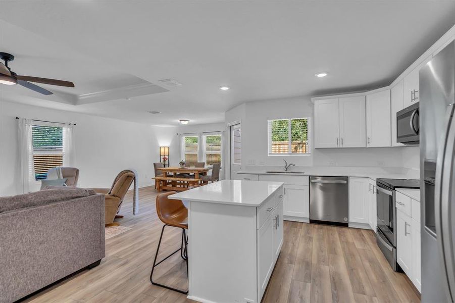 Kitchen with open floor plan, white cabinets, appliances with stainless steel finishes, a center island, and a breakfast bar