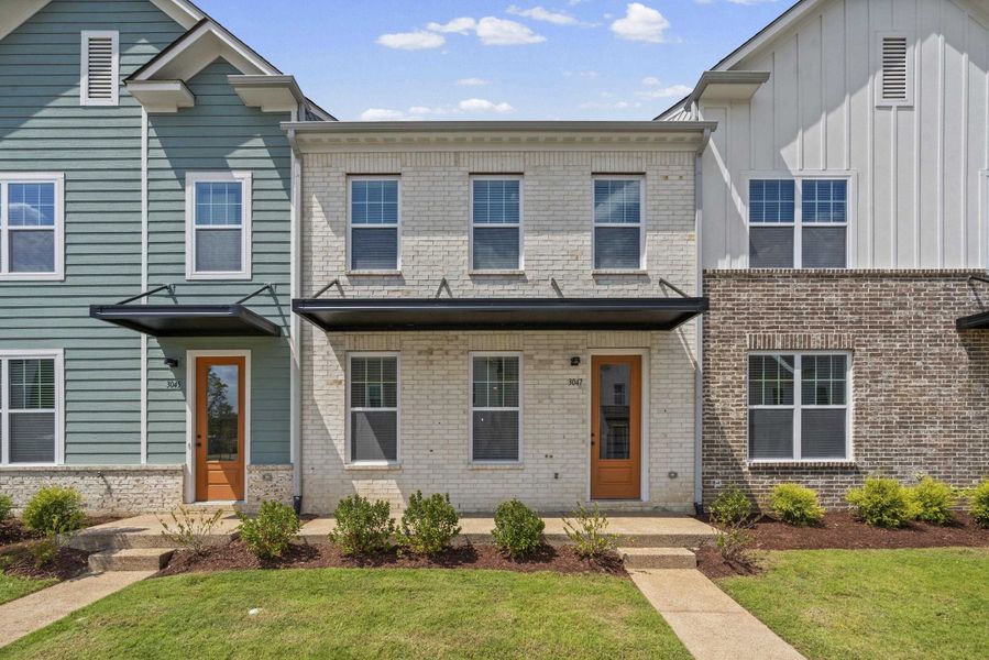 White brick facade with black metal awnings, framed by a wood-finish front door