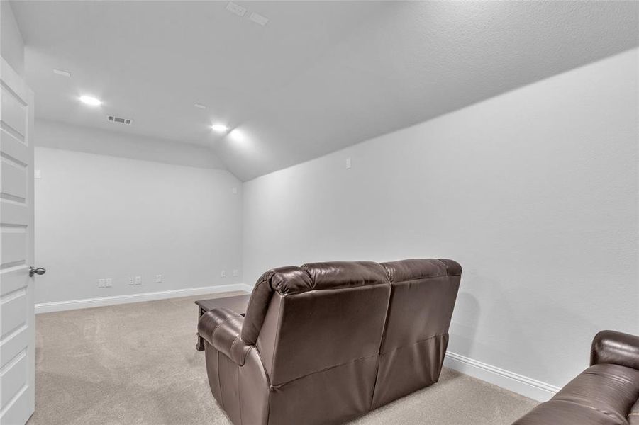 Cinema room featuring vaulted ceiling, baseboards, visible vents, and light colored carpet