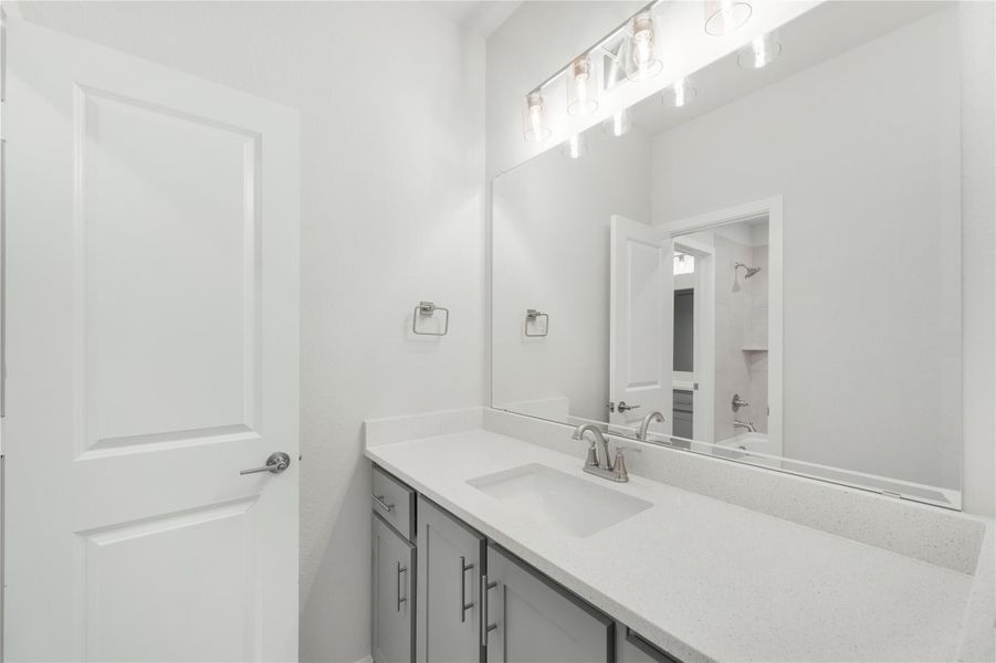 Bathroom vanity with gray cabinets, white quartz countertop, single sink, and large mirror with overhead lighting.