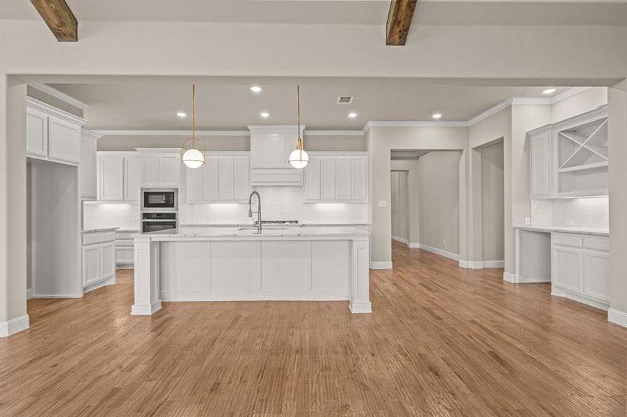 Kitchen featuring tasteful backsplash, beam ceiling, white cabinetry, an island with sink, and recessed lighting